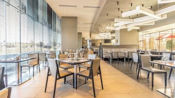 Um restaurante moderno com mesas e cadeiras altas, grandes janelas e luminárias contemporâneas.