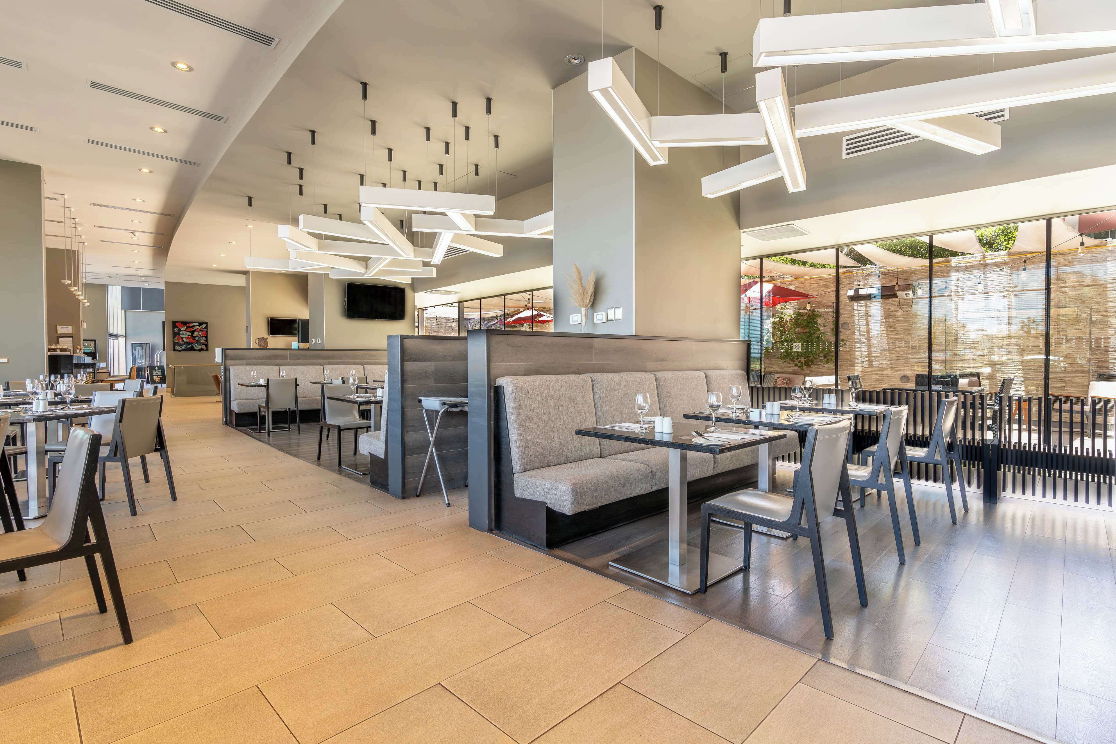 A modern restaurant with high ceilings, contemporary lighting fixtures, and a mix of seating arrangements including tables and booths.