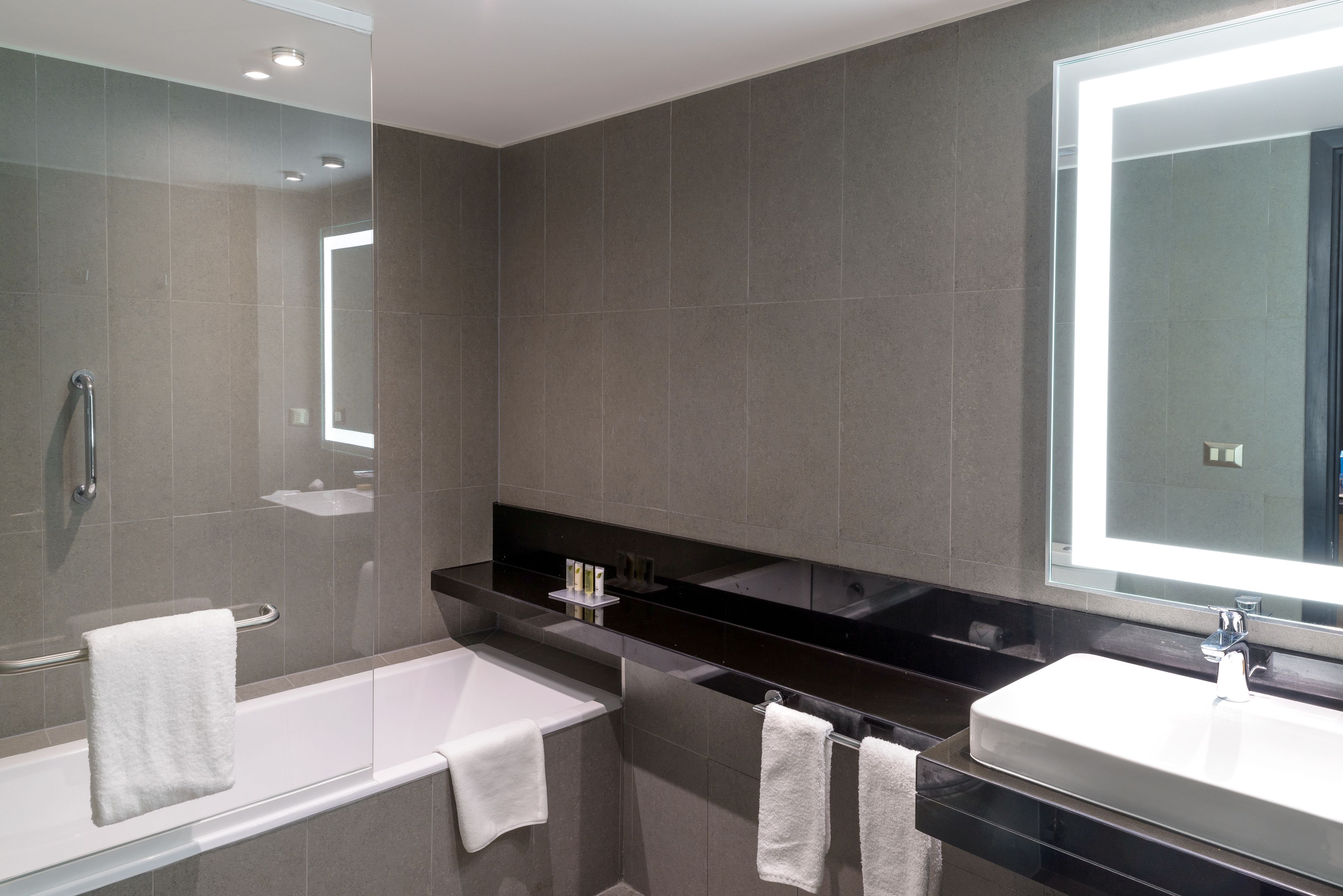 A modern bathroom with a glass-enclosed shower, a white bathtub, and a black countertop with a sink and mirror.