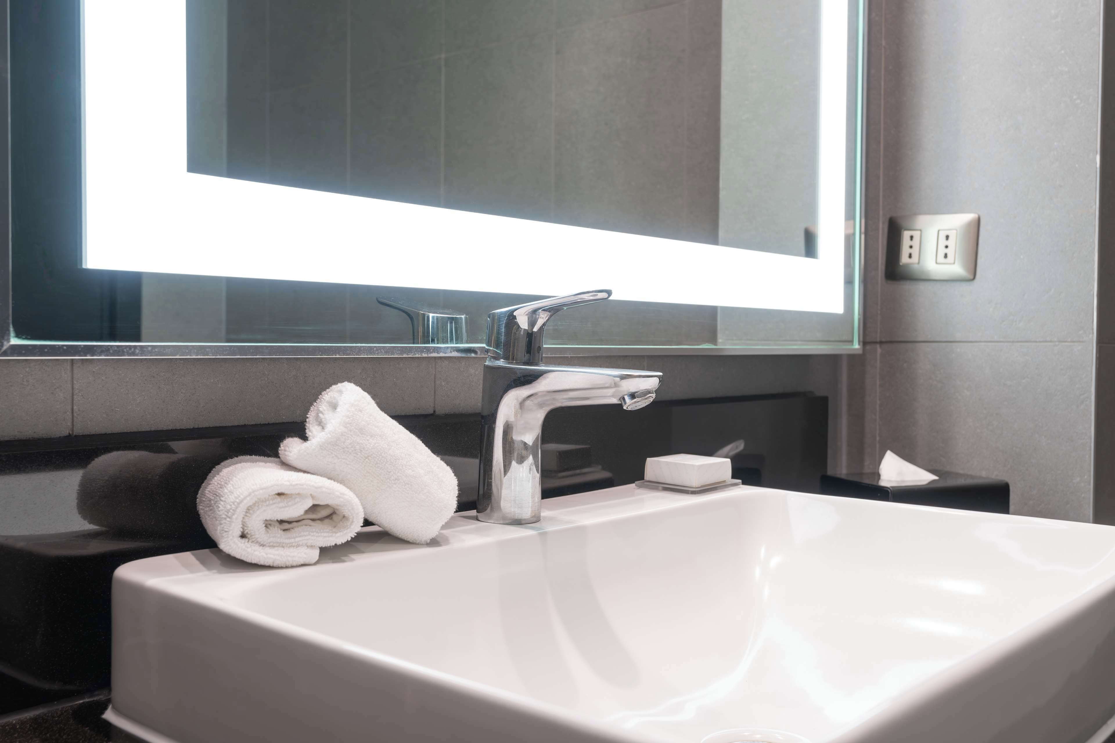 Un baño moderno con un lavabo blanco, un espejo y una toalla en la encimera.