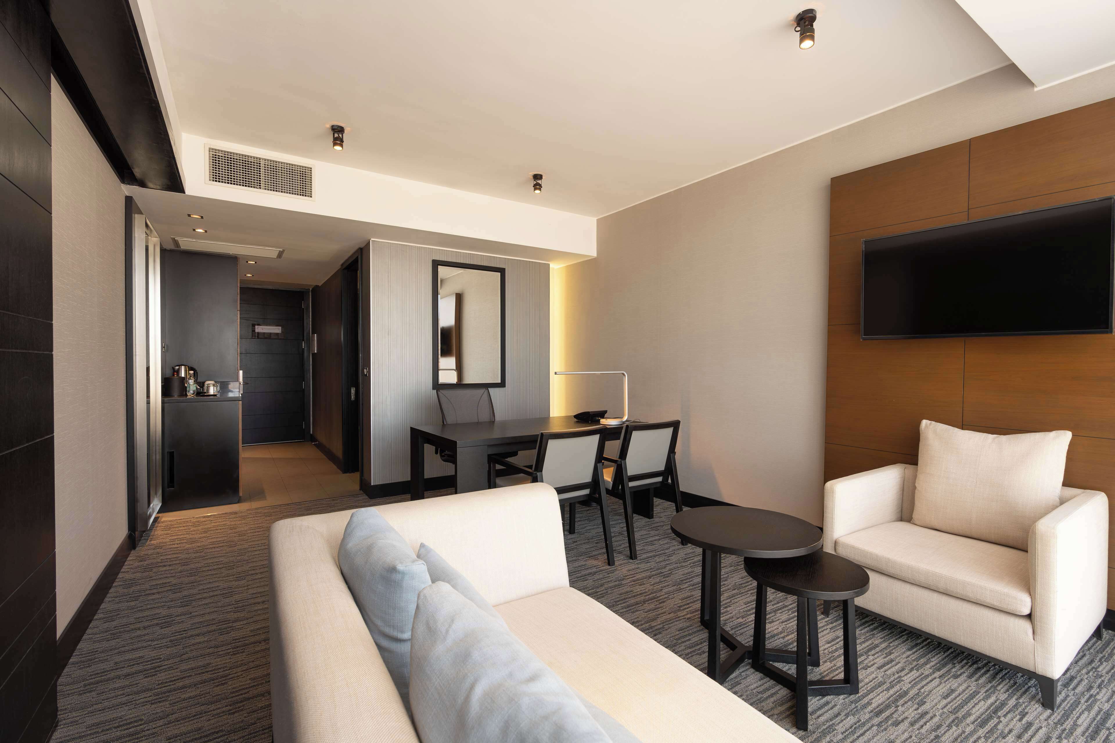 Une chambre d’hôtel moderne équipée d’un canapé, d’un fauteuil et d’un téléviseur à écran plat fixé au mur.