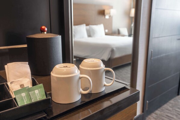 A hotel room with a bed, a nightstand, a coffee maker, and a tray with a tissue box and a green packet.
