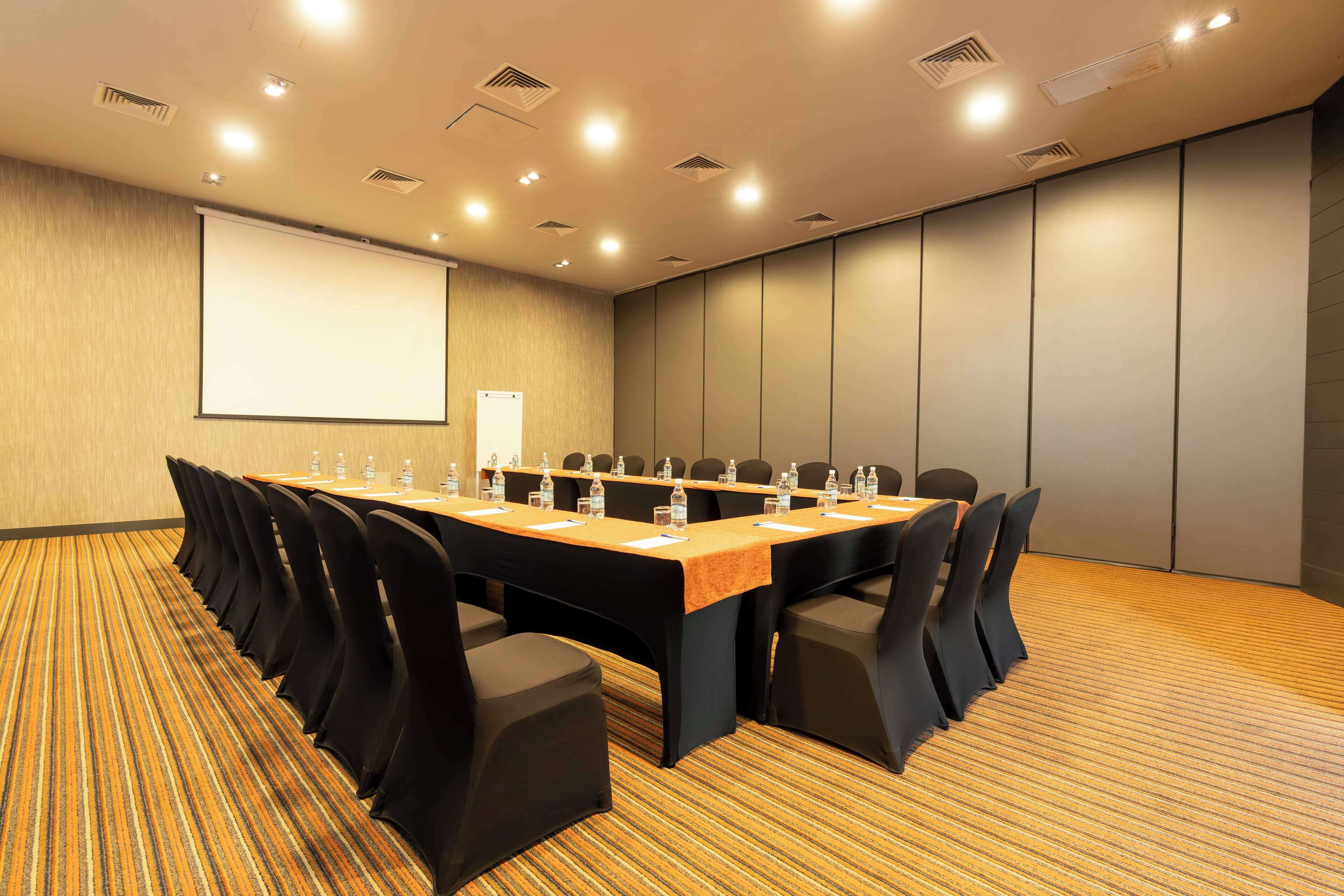 A conference room with a long table, chairs, a projector screen, and a carpeted floor.