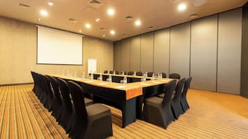 A conference room with a long table, chairs, a projector screen, and a carpeted floor.
