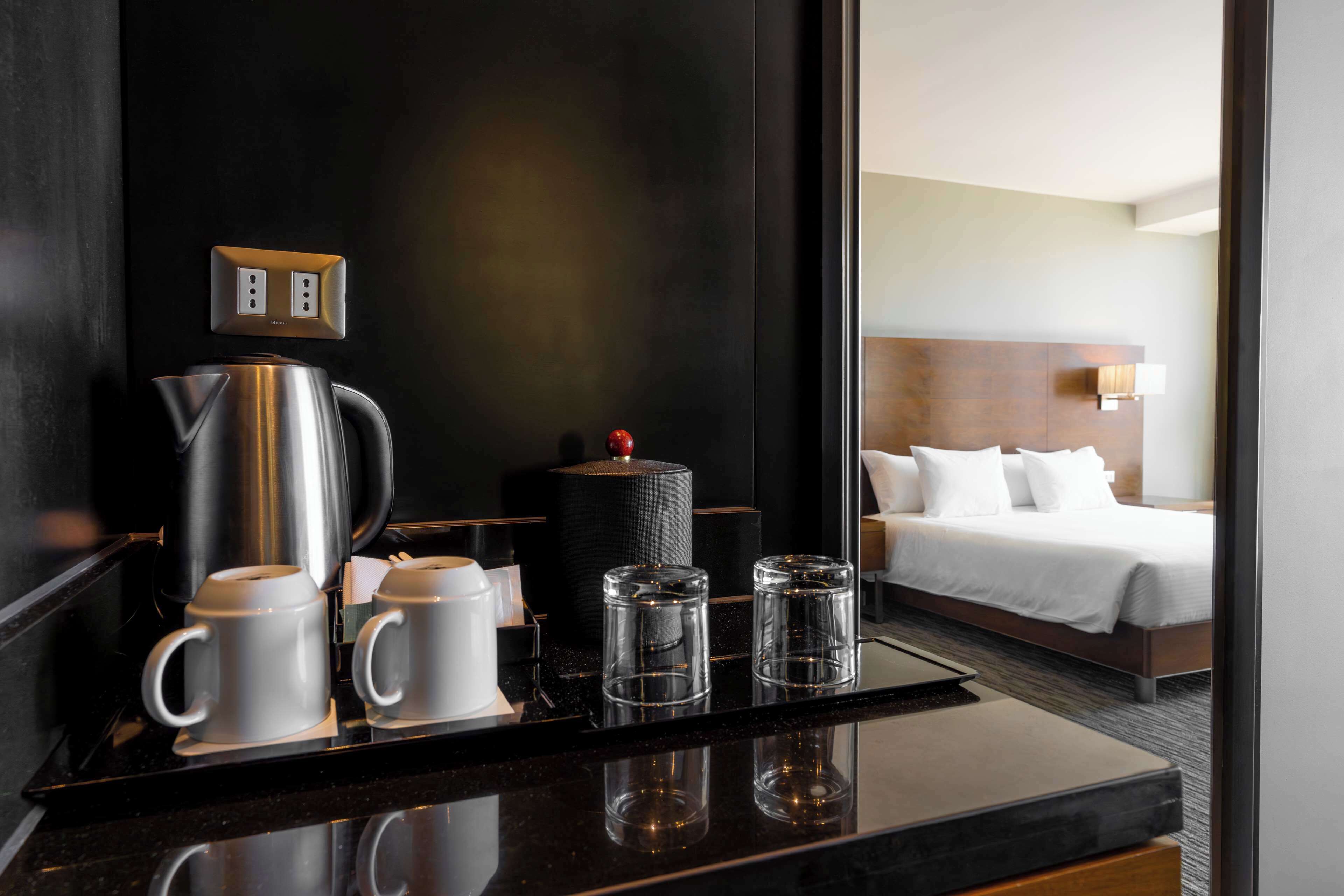 Et hotelværelse med en seng, et natbord med elkedel, kopper og glas.