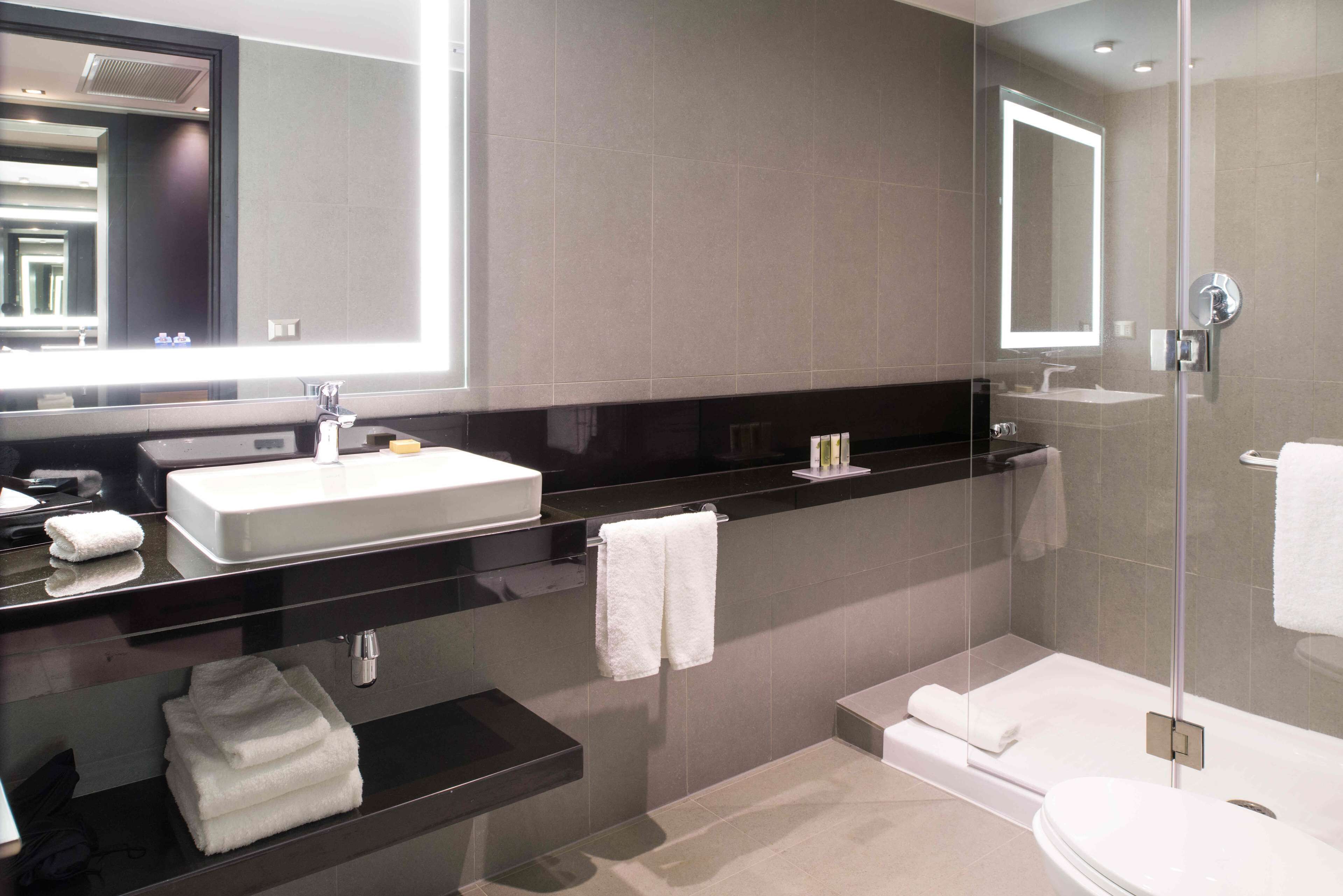 A modern bathroom with a large mirror, a white sink, a black countertop, a glass-enclosed shower, and a toilet.
