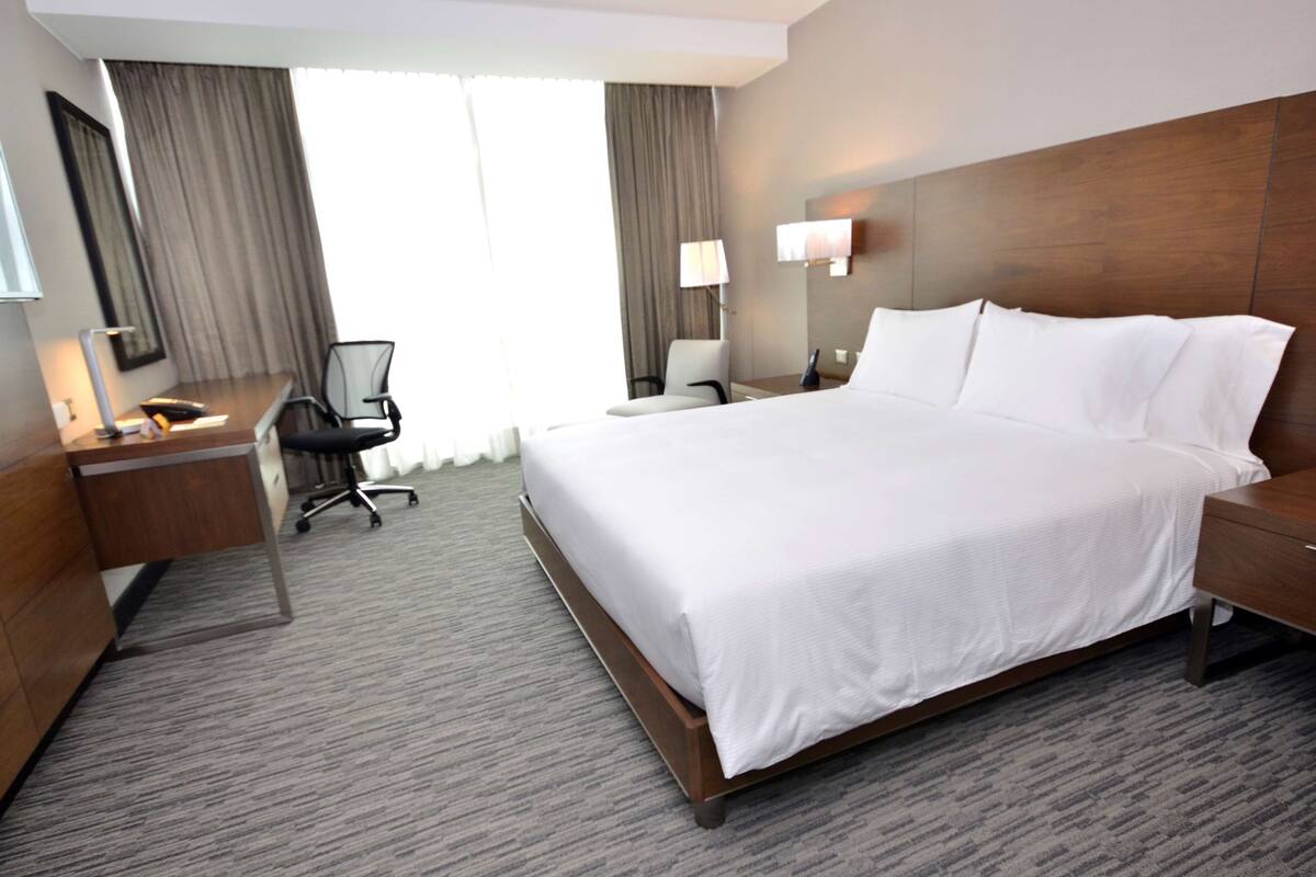 A hotel room with a large bed, a desk, a chair, a lamp, and a nightstand.