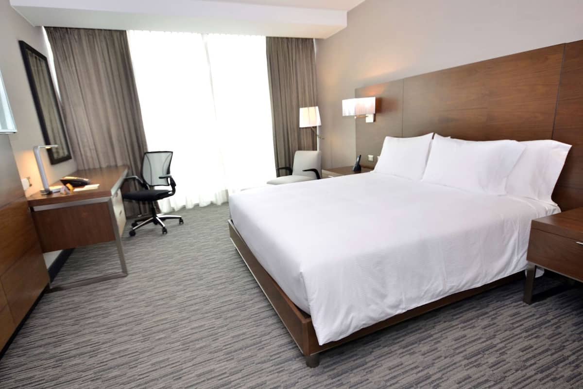 A hotel room with a large bed, a desk, a chair, a lamp, and a nightstand.