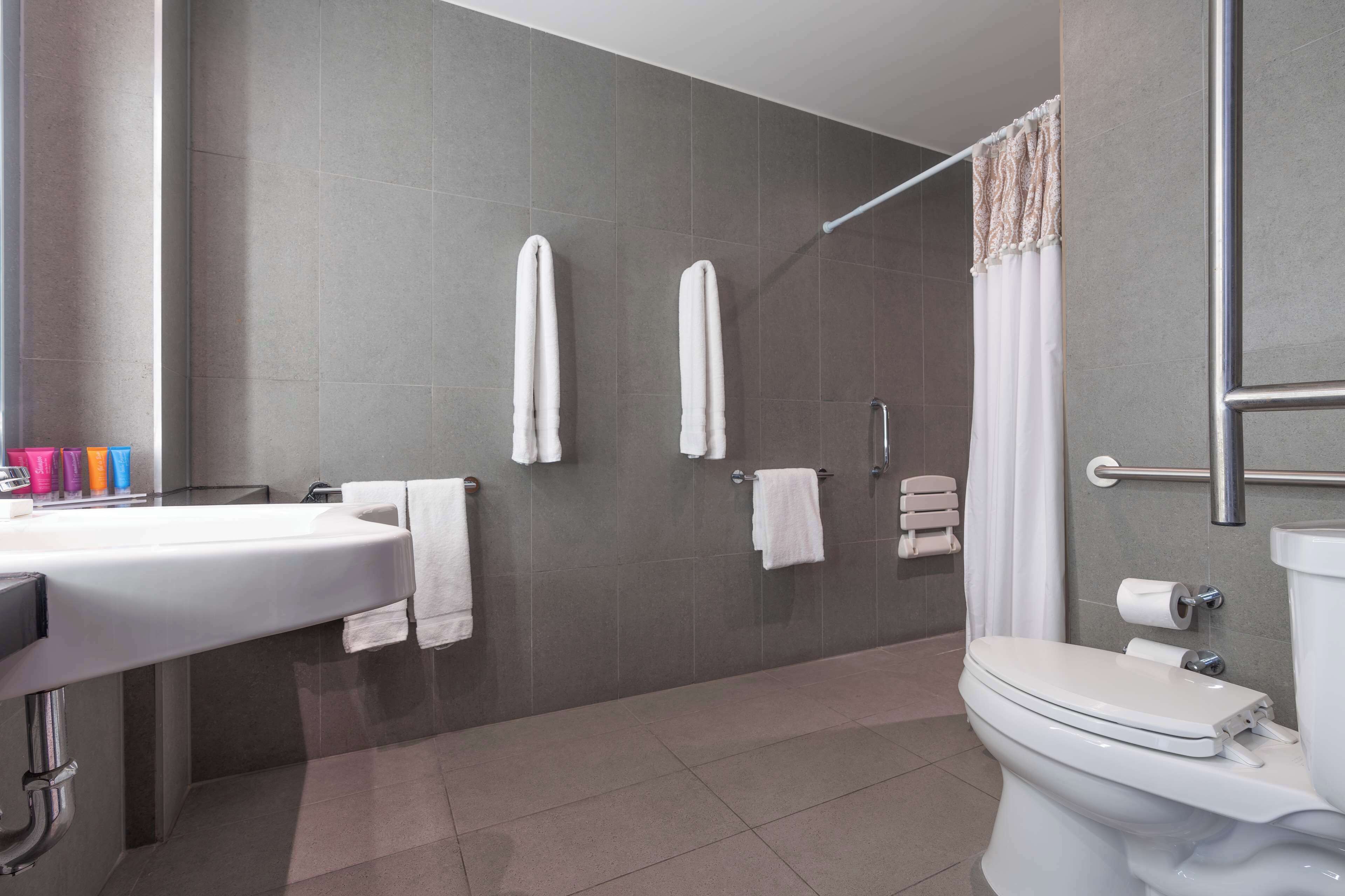 Un baño moderno con un lavamanos grande, dos toallas blancas, una cortina de ducha y un inodoro.