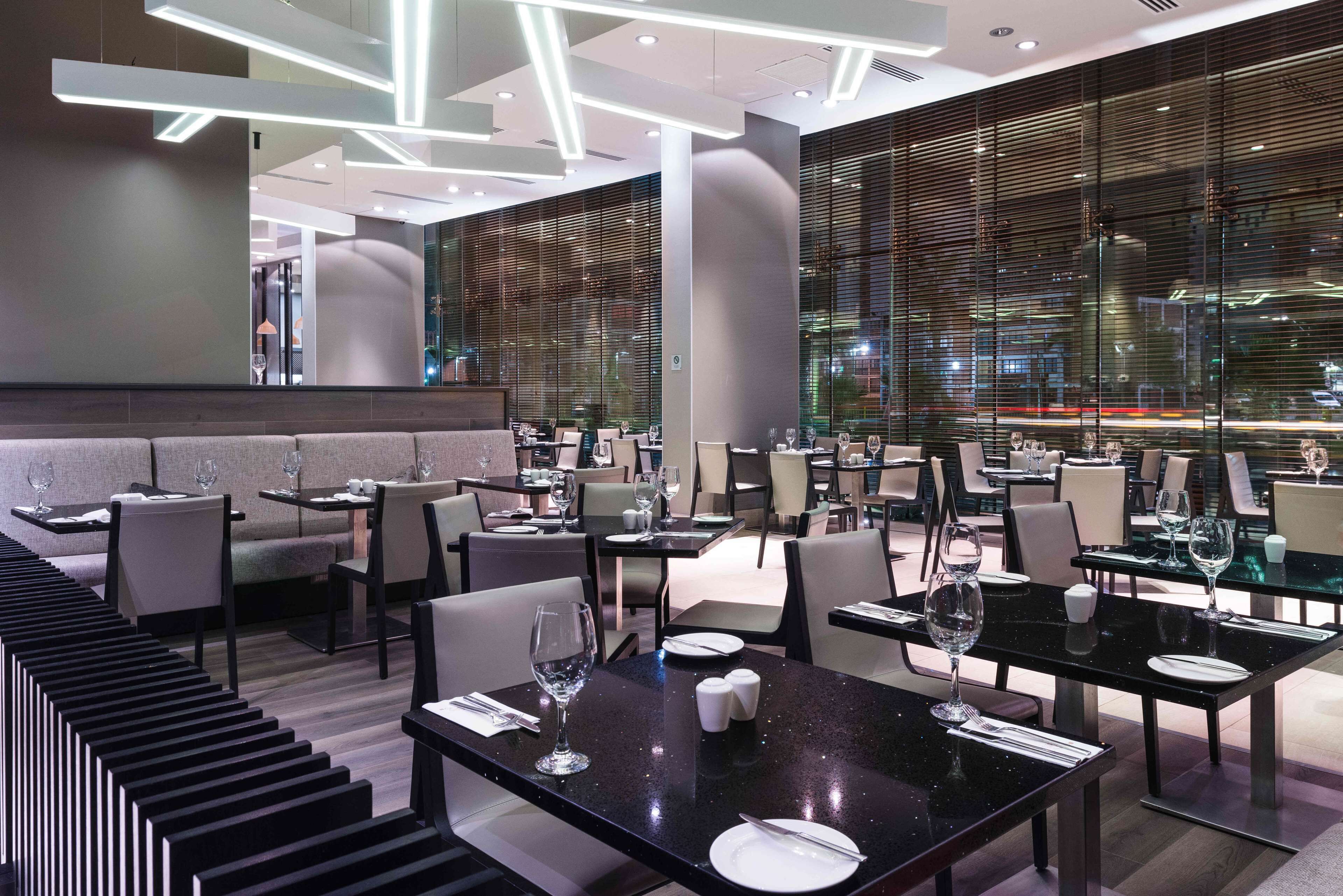 A modern restaurant with black marble tables, white plates, and wine glasses set.