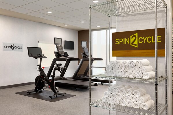 Un gimnasio con bicicletas estáticas, cintas de correr y una pantalla instalada en la pared.