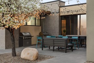 Un patio exterior con una parrilla, zona de estar y luces colgantes.