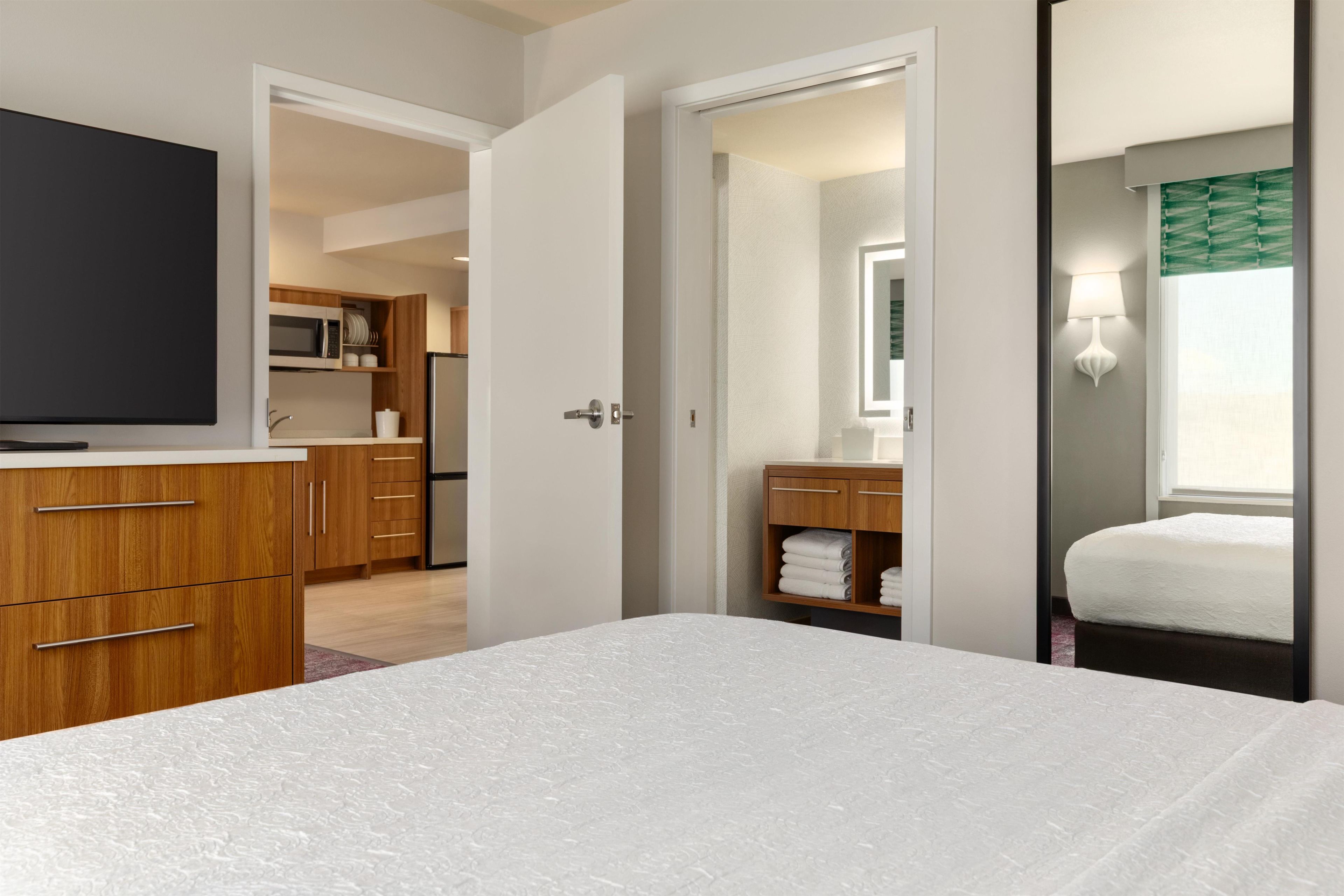 A hotel room with a bed, a TV, a wardrobe, a bathroom with a mirror, and a shower area.