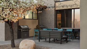 An outdoor patio with a grill, seating, and string lights.
