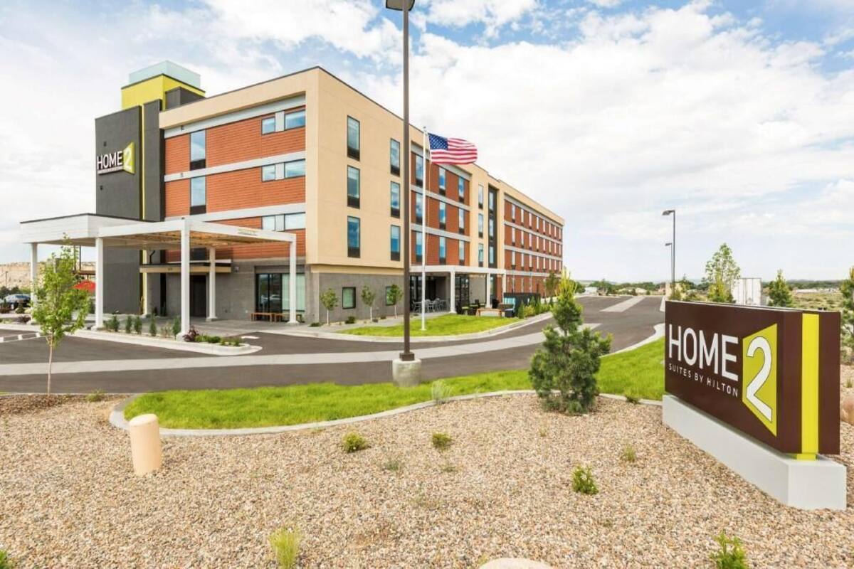 Een modern hotelgebouw met een bord waarop 'HOME 2 Suites by Hilton' staat, met een gevel van baksteen, veel ramen en een Amerikaanse vlag.