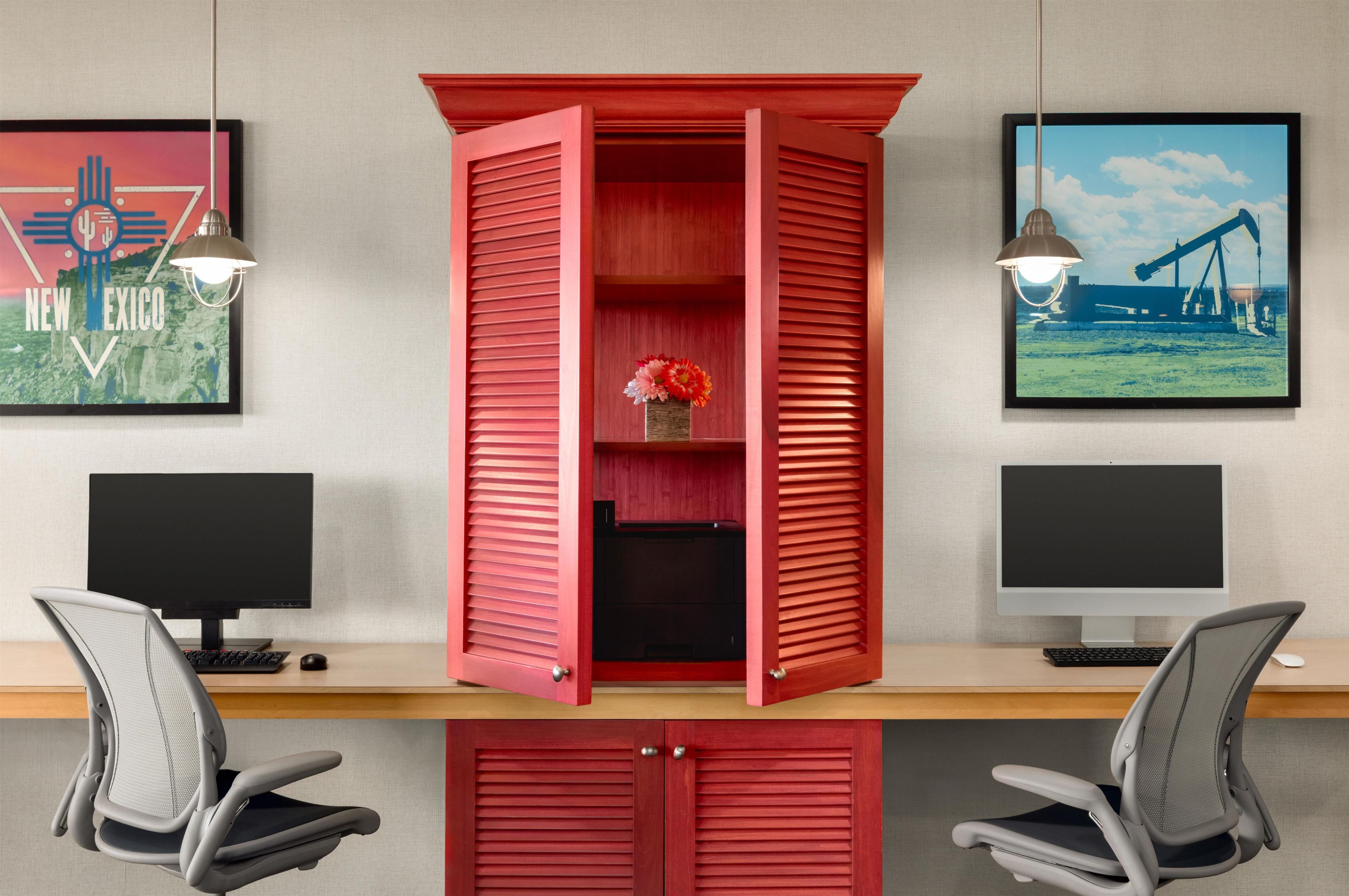 A workspace with two computer monitors, a red cabinet with a flower arrangement, and two chairs.