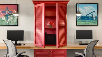 A workspace with two computer monitors, a red cabinet with a flower arrangement, and two chairs.