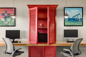 A workspace with two computer monitors, a red cabinet with a flower arrangement, and two chairs. - Home2 Suites by Hilton Farmington/Bloomfield (Farmington)