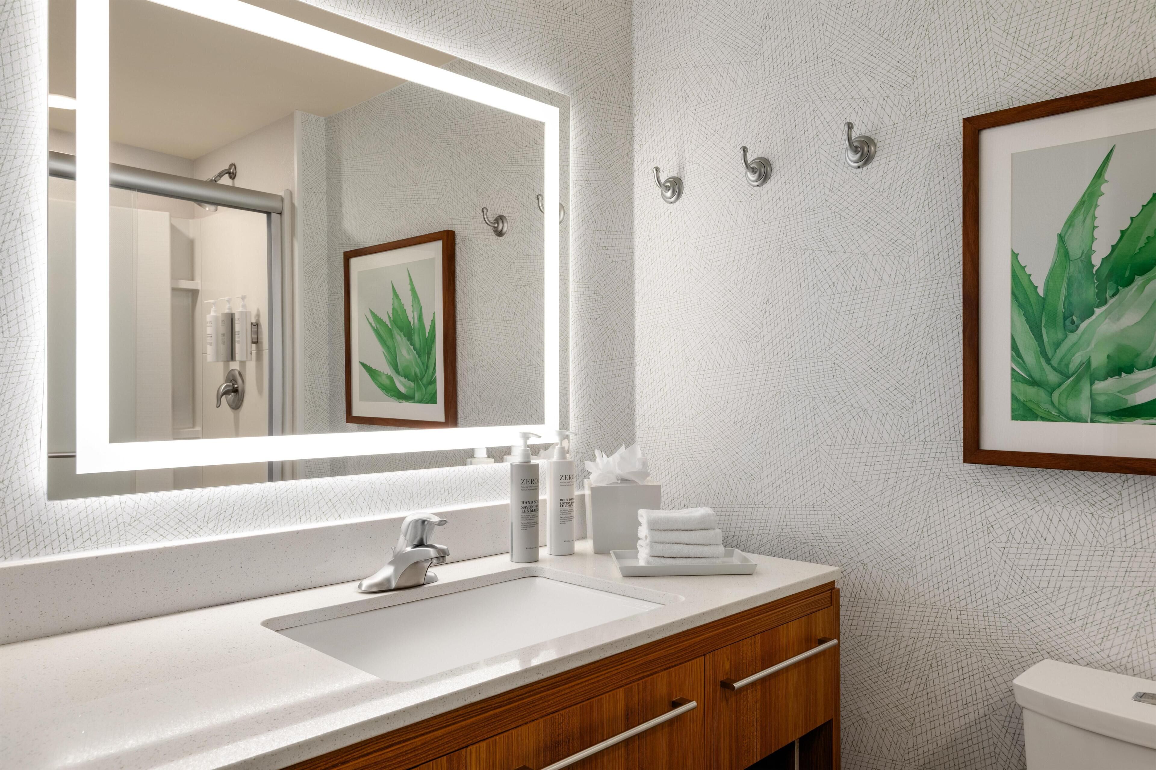 A bathroom with a large mirror, a sink, wooden vanity, and a framed plant.