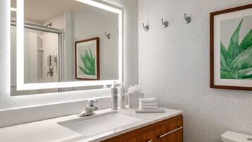 A bathroom with a large mirror, a sink, wooden vanity, and a framed plant.