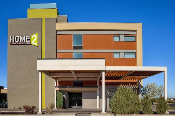 A modern hotel building with a 'HOME 2' sign, a covered entrance, and a clear blue sky.