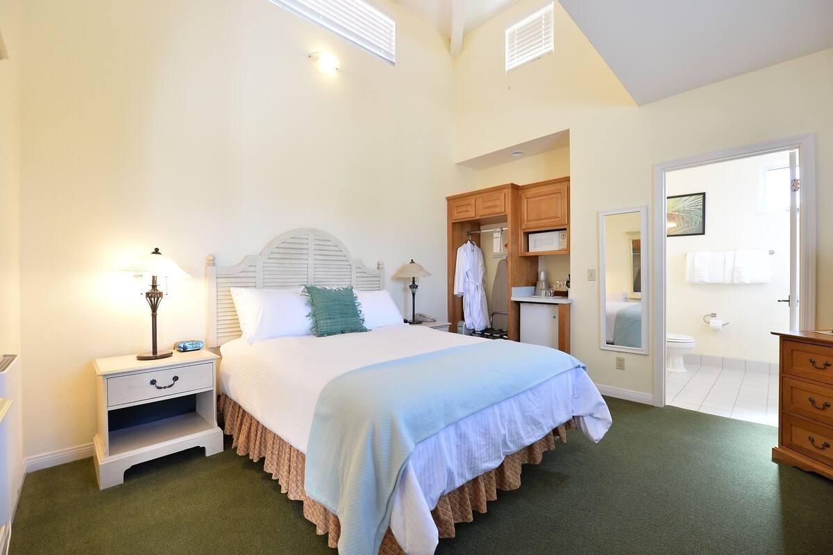 A bedroom with a bed, nightstand, dresser, and a view of the bathroom.