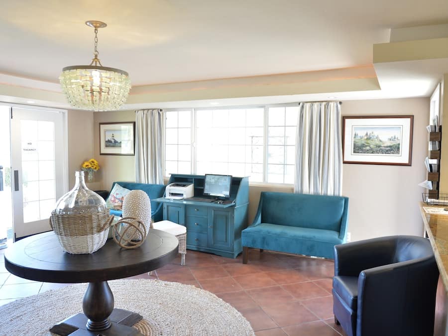 A spacious living room with a blue sofa, a round table with a vase, and a computer on a desk.