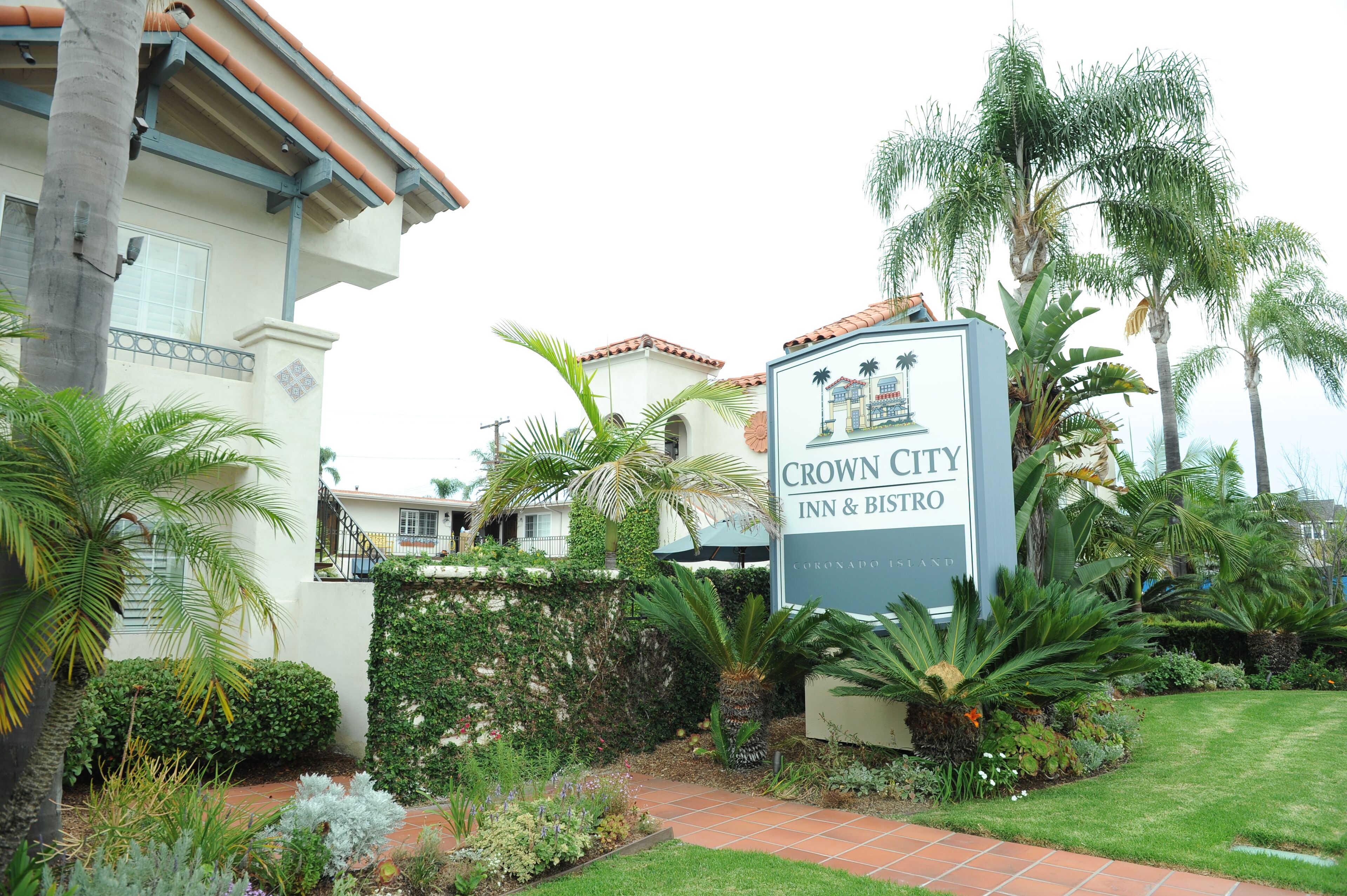 A sign for Crown City Inn & Bistro surrounded by lush greenery and palm trees.