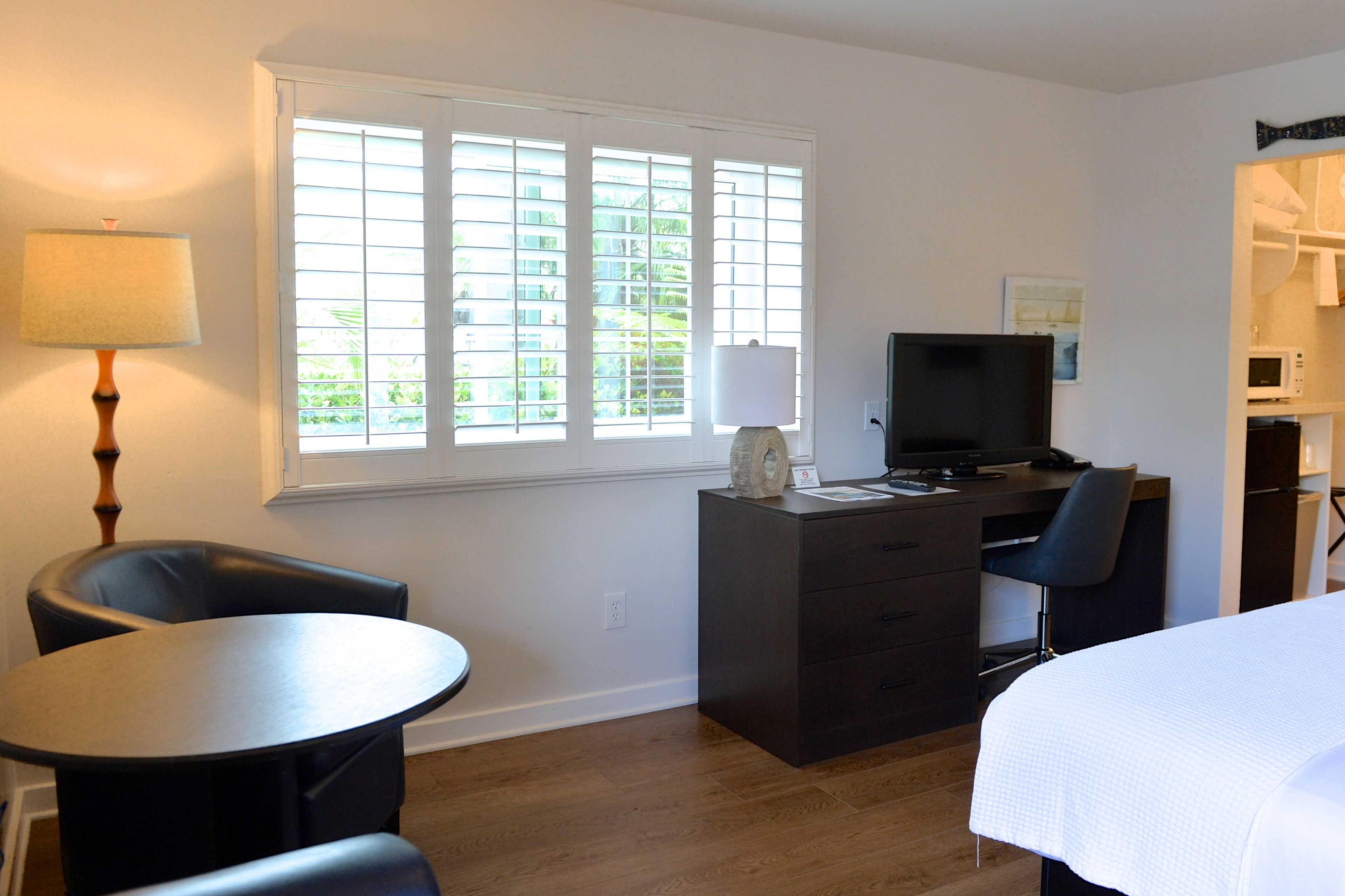 A hotel room with a desk, a chair, a bed, a TV, and a window with blinds.