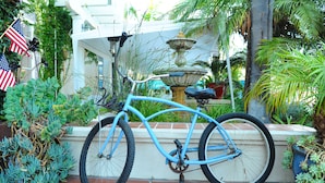 Een blauwe fiets geparkeerd op een betegeld terras, met een fontein en planten op de achtergrond.