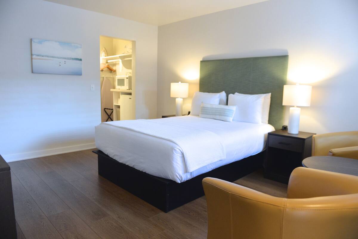 A hotel room with a large bed, two bedside tables with lamps, a chair, and a painting on the wall.