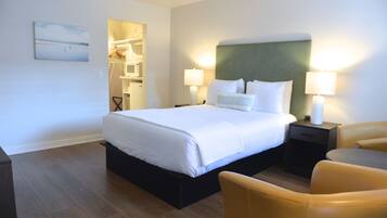 Un cuarto de hotel con una cama grande, dos mesitas de noche con lámparas, una silla y un cuadro en la pared.