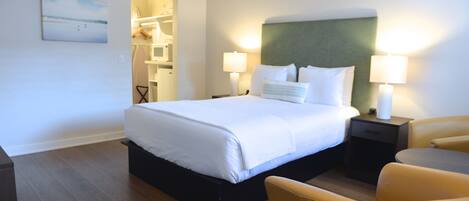 Un cuarto de hotel con una cama grande, dos mesitas de noche con lámparas, una silla y un cuadro en la pared.