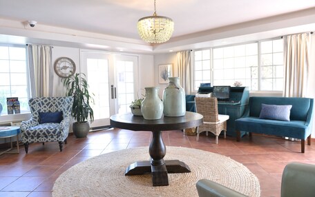 A living room with a round table, a blue sofa, a patterned armchair, and a potted plant.