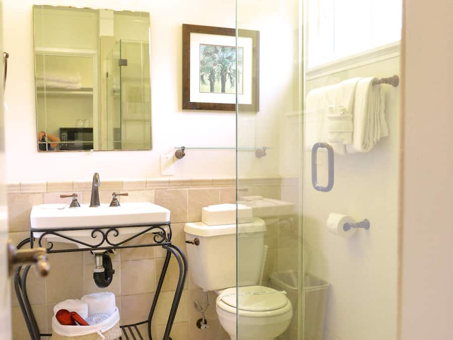 A bathroom with a glass-enclosed shower, a sink with a metal frame, a toilet, and a mirror above the sink.