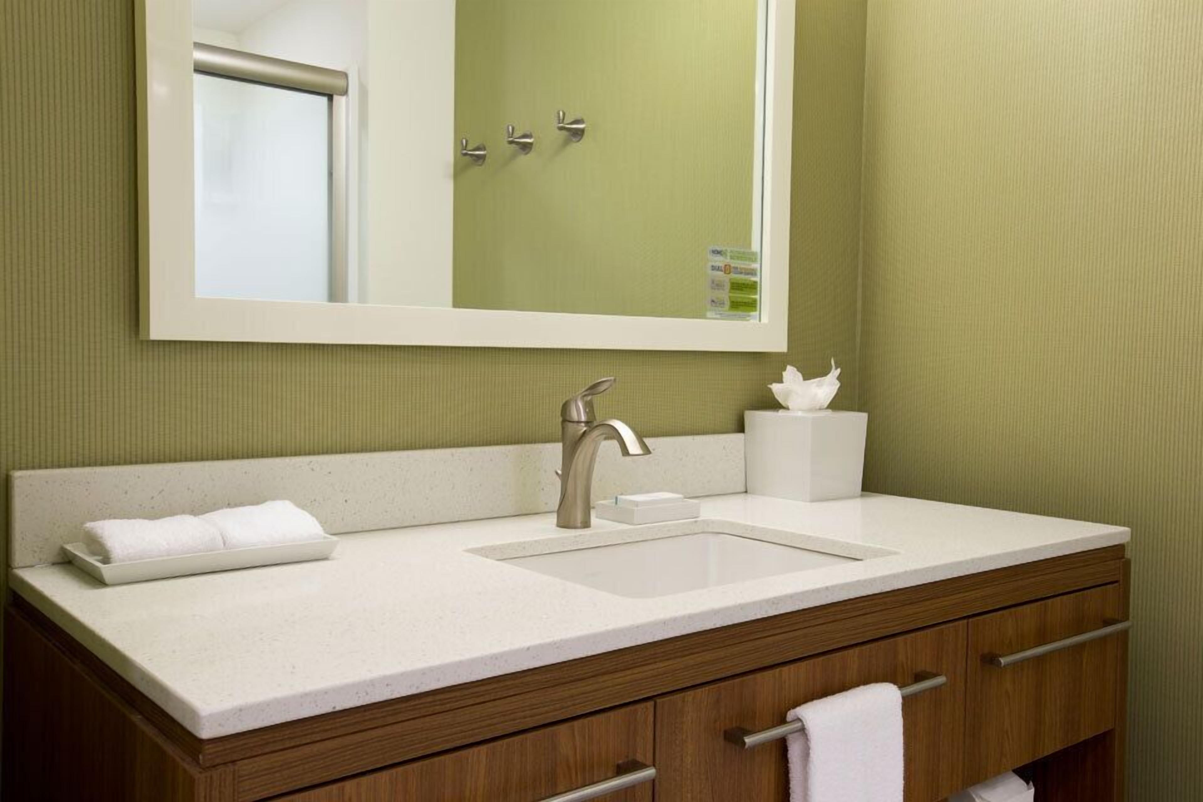 Un baño con lavamanos blanco, espejo y tocador de madera con cajones.