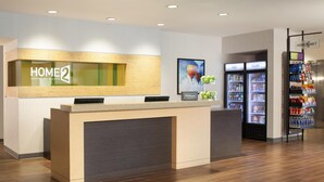 Un espace d’accueil d’hôtel comprenant un comptoir de réception, un écran numérique, un réfrigérateur contenant des boissons et un distributeur automatique.