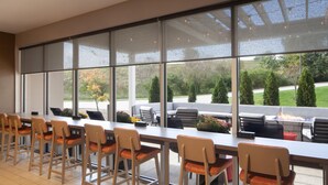 Un vaste espace extérieur aménagé pour les repas, avec une longue table et de nombreuses chaises, ainsi que de grandes fenêtres offrant une vue sur le paysage environnant.