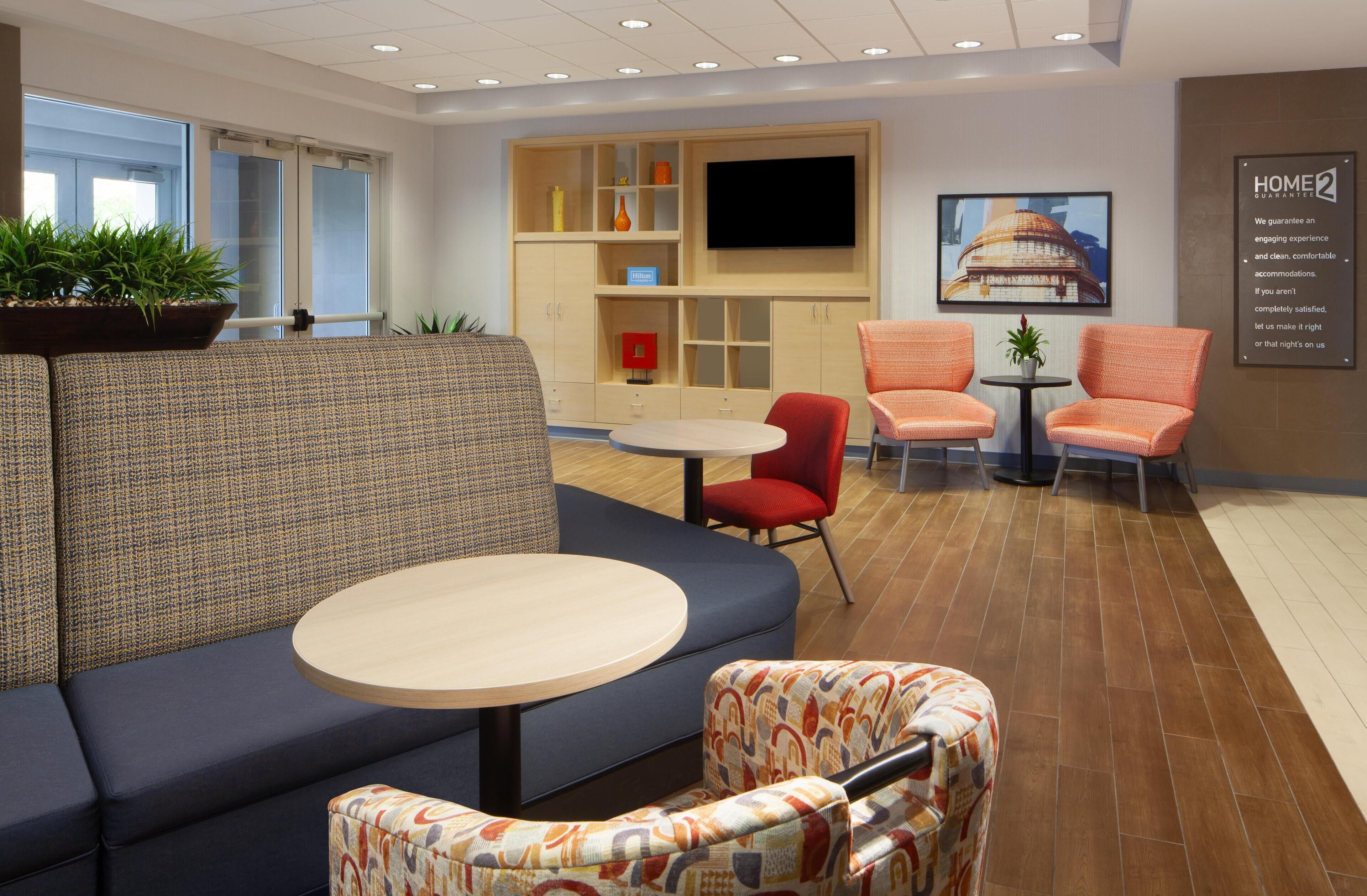 A modern hotel lobby with a sofa, chairs, a small table, and a TV mounted on the wall.