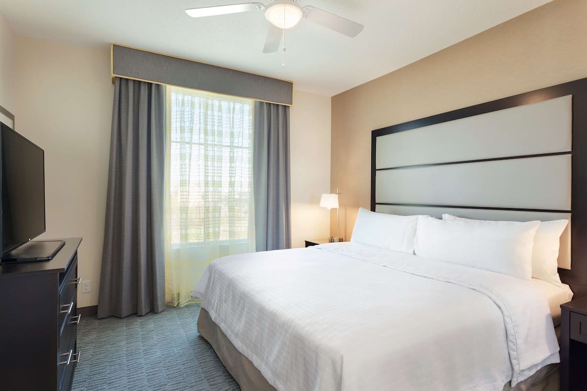 Une chambre d’hôtel équipée d’un lit, d’une télévision, d’un bureau, d’une lampe et d’un ventilateur de plafond.