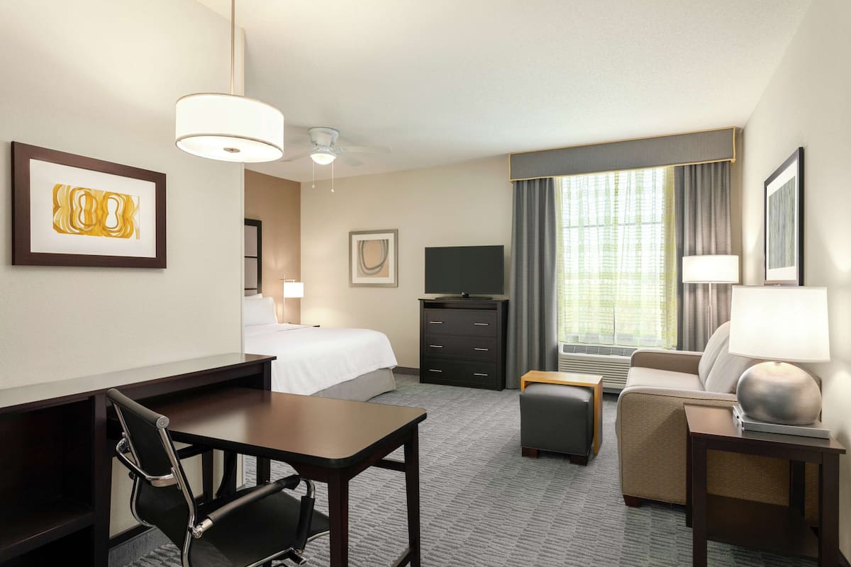 Une chambre d’hôtel avec un lit, un bureau, une chaise, une télévision et un canapé.