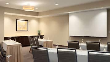 A conference room with tables, chairs, a projector screen, and a framed picture on the wall.