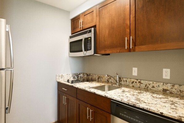 A kitchen with wooden cabinets, a stainless steel microwave, a dishwasher, and a granite countertop.