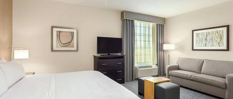 A hotel room with a large bed, a sofa, a TV, and a desk.