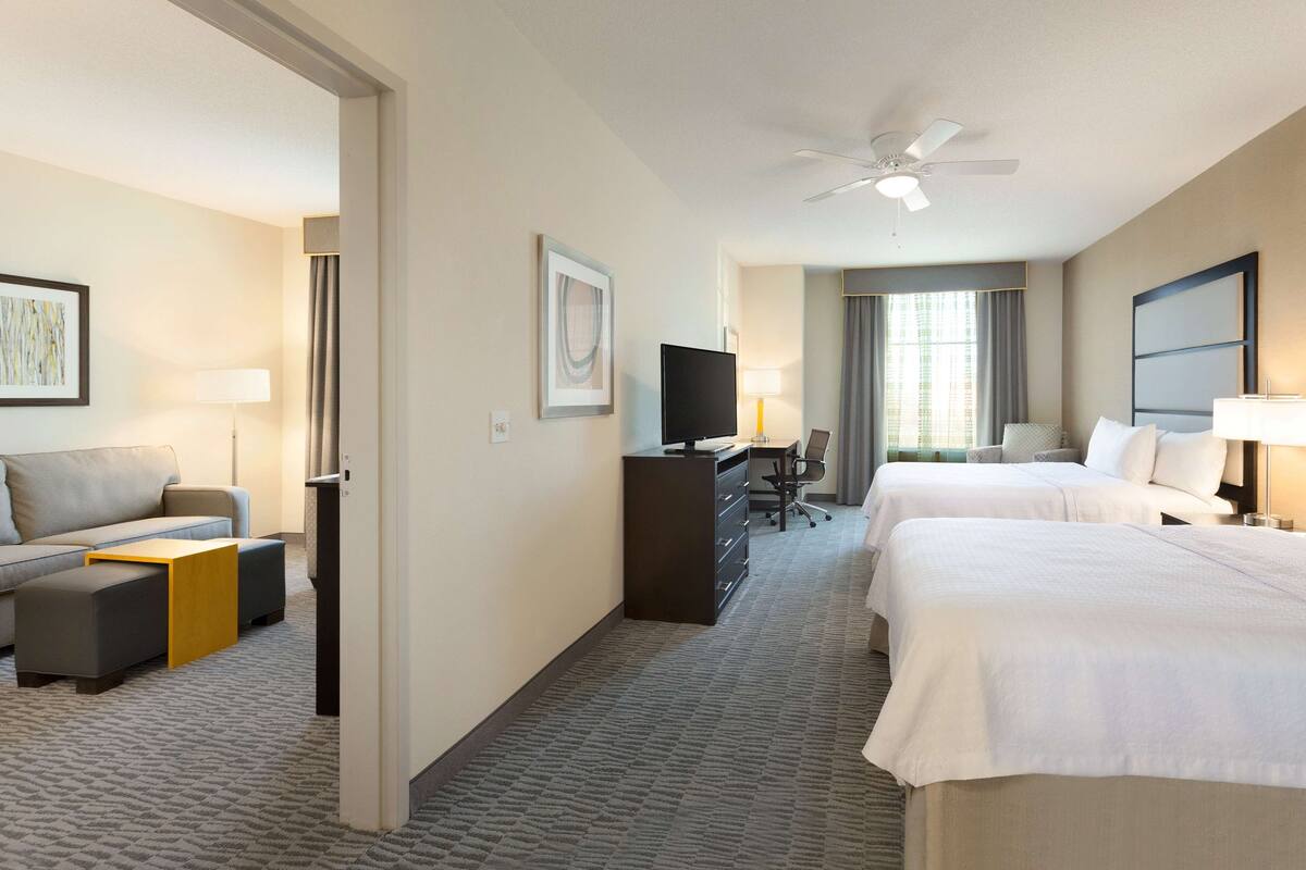 Une chambre d’hôtel avec deux lits, un canapé, un bureau, une télévision et un ventilateur de plafond.