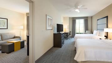 A hotel room with two beds, a sofa, a desk, a television, and a ceiling fan.