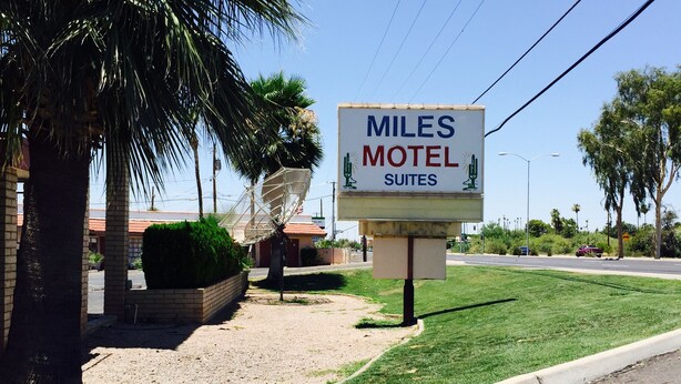 A sign for Miles Motel Suites with a satellite dish and palm trees in the background.