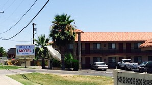 A motel with a signboard, a parking lot, and a building with a red-tiled roof.