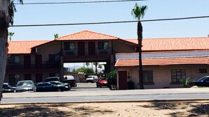 A two-story building with a red-tiled roof, a parking lot with several cars, and a palm tree in the foreground.