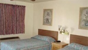 A room with two beds, a nightstand, and a wall-mounted lamp.